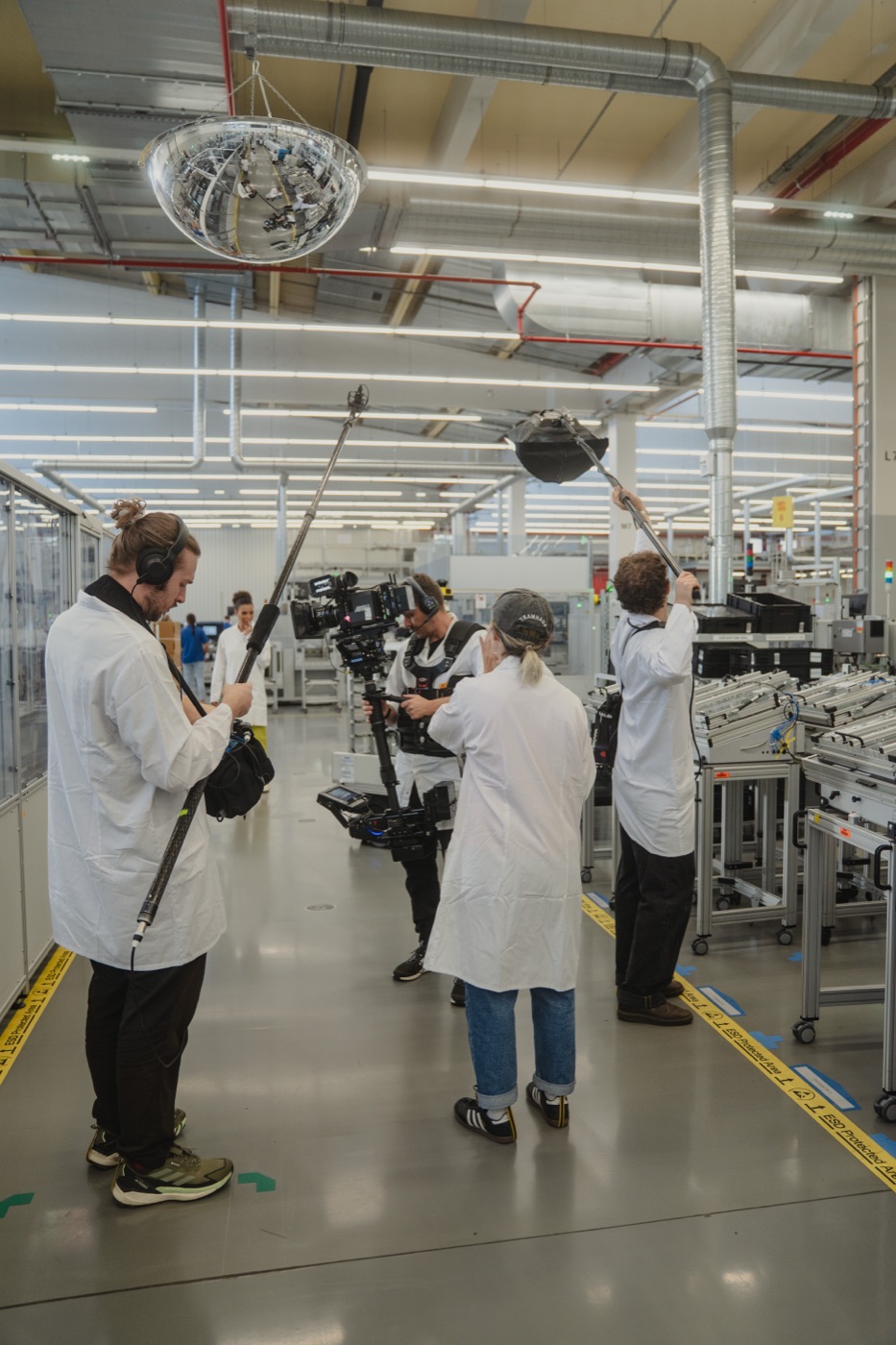 Industriedreh in einer Fertigungshalle: zwei Tonangeln über der Linie, Kamerateam in der Mitte.