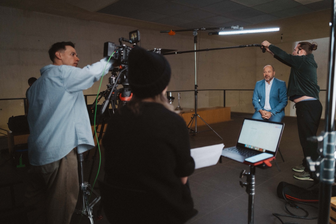 Interviewsetup in einem Betonraum: Kamera, Licht und Tonangel über dem Interviewgast im blauen Sakko.