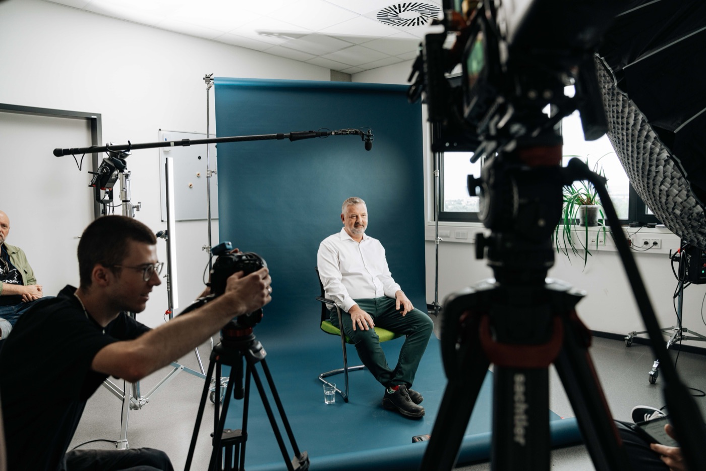 Corporate-Interview: Interviewgast vor blauem Hintergrund zwischen zwei Kameras, Tonangel über dem Set.